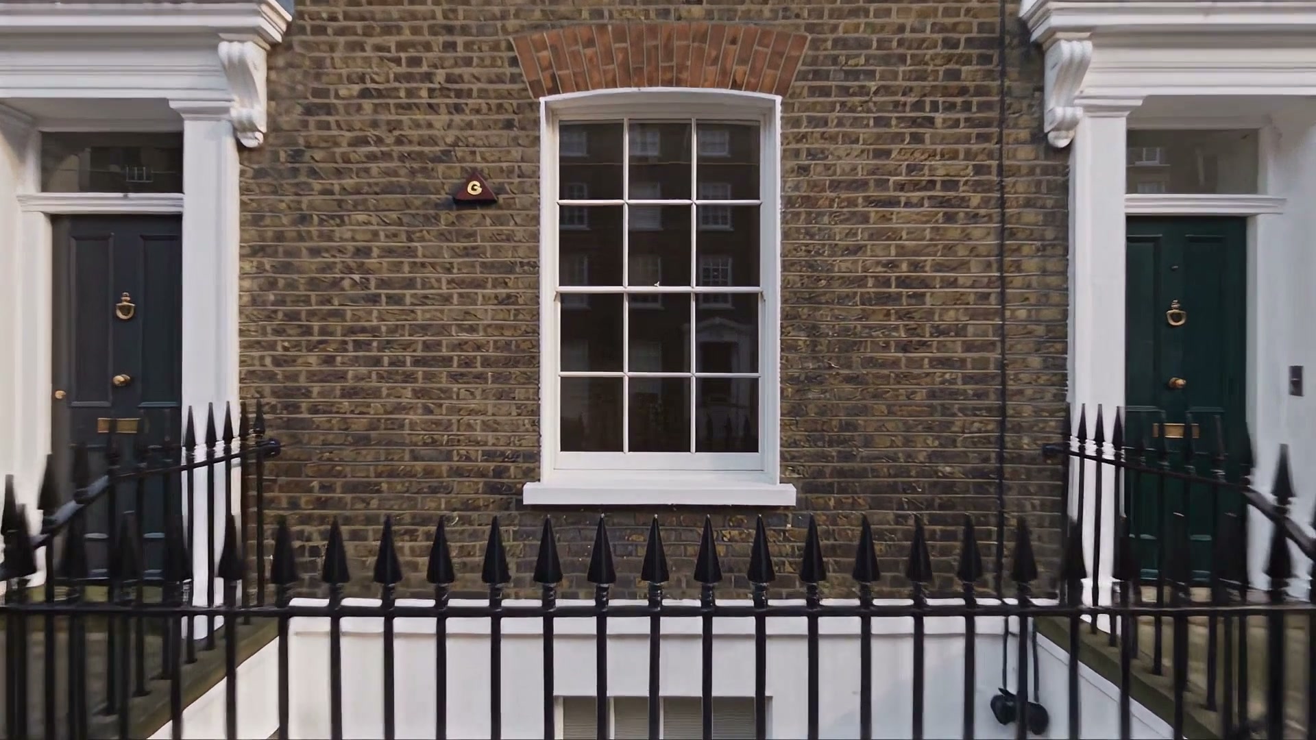 The brick facade of a Georgian terrace with a white sash window between two front doors