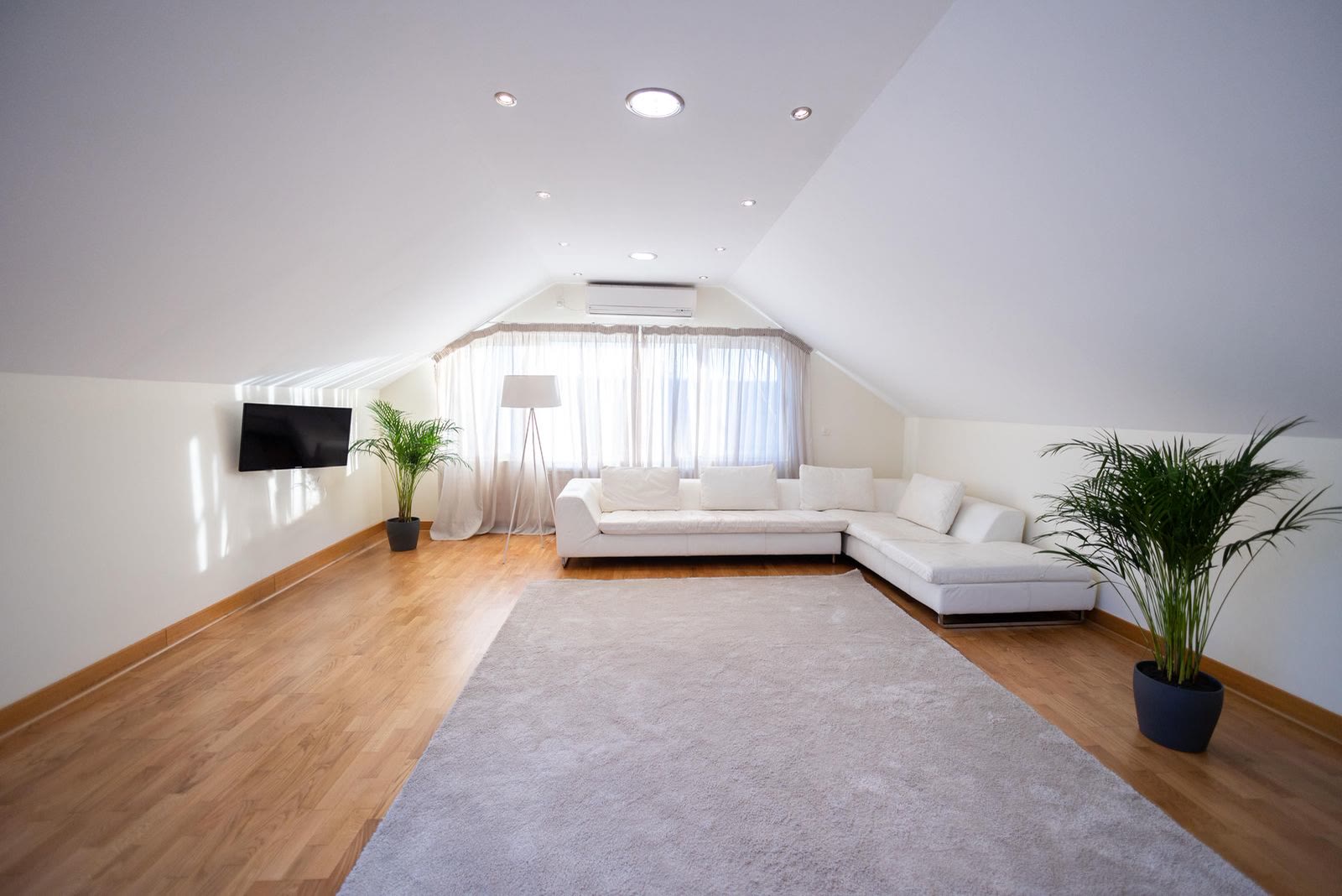 A spacious attic living room with a white sofa and a hardwood floor