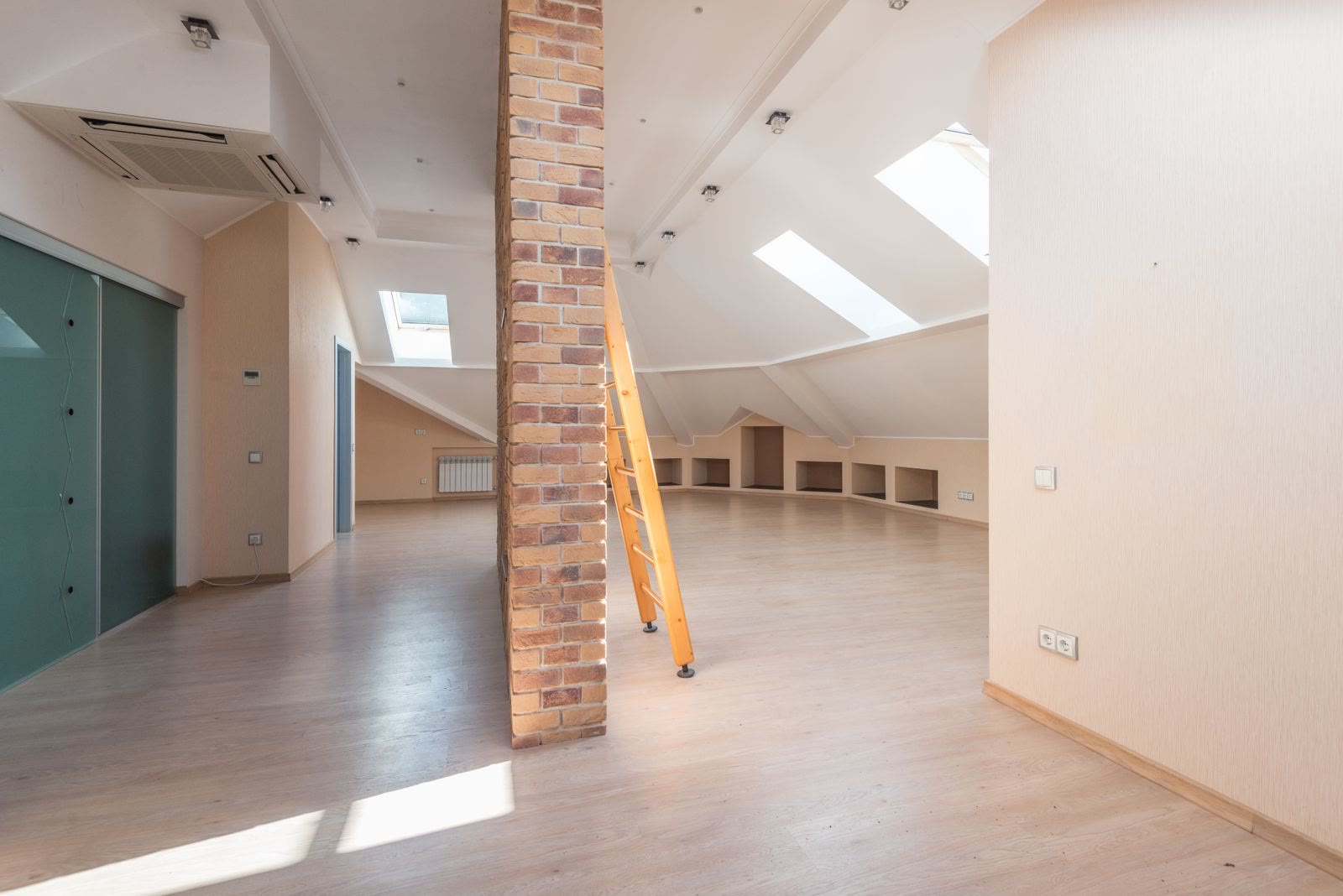 A converted attic with skylights, a brick pillar and a wooden floor