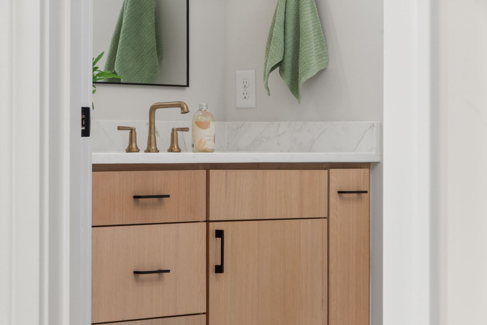 A bathroom vanity with wooden cabinets, a stone top and brass fixtures