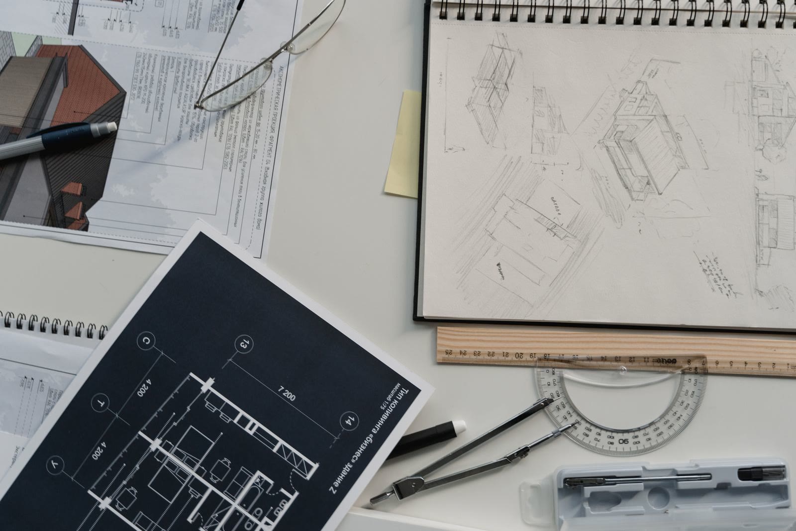 Architectural sketches and floor plans spread on a desk with pencils and a scale ruler