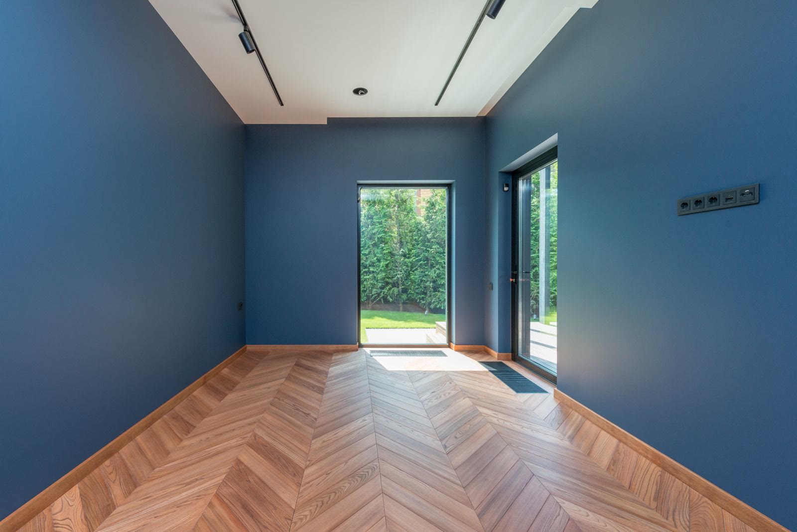A room with blue walls and a herringbone floor opening through glass doors to a garden