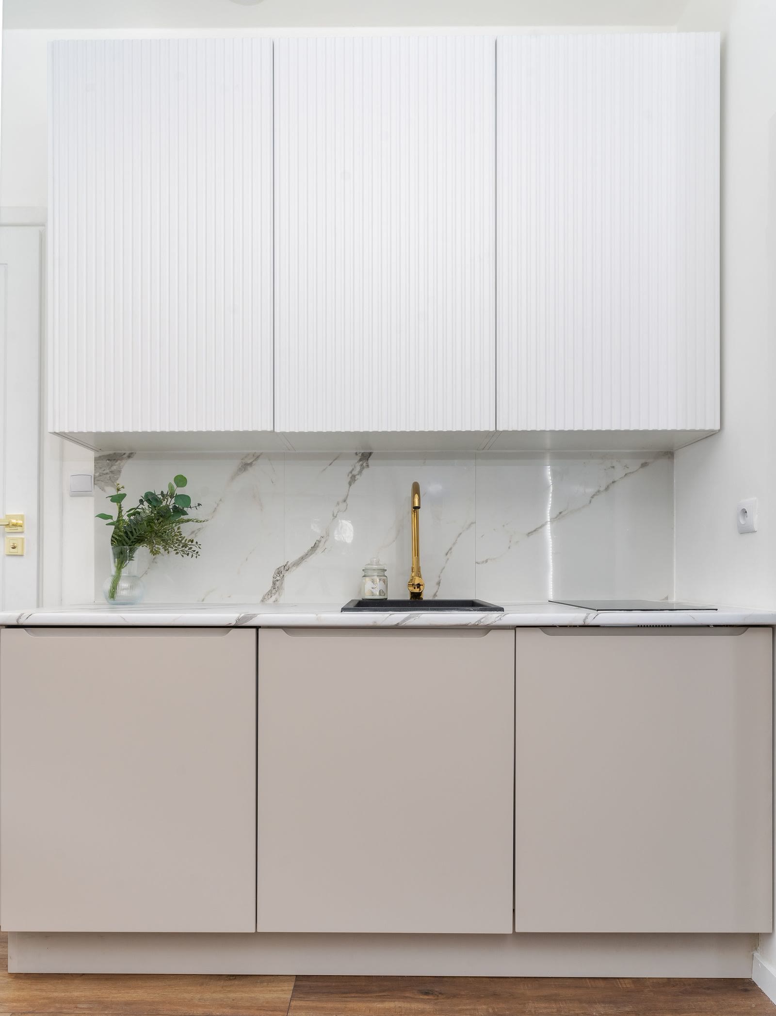 A minimalist kitchen with a marble splashback and a golden tap