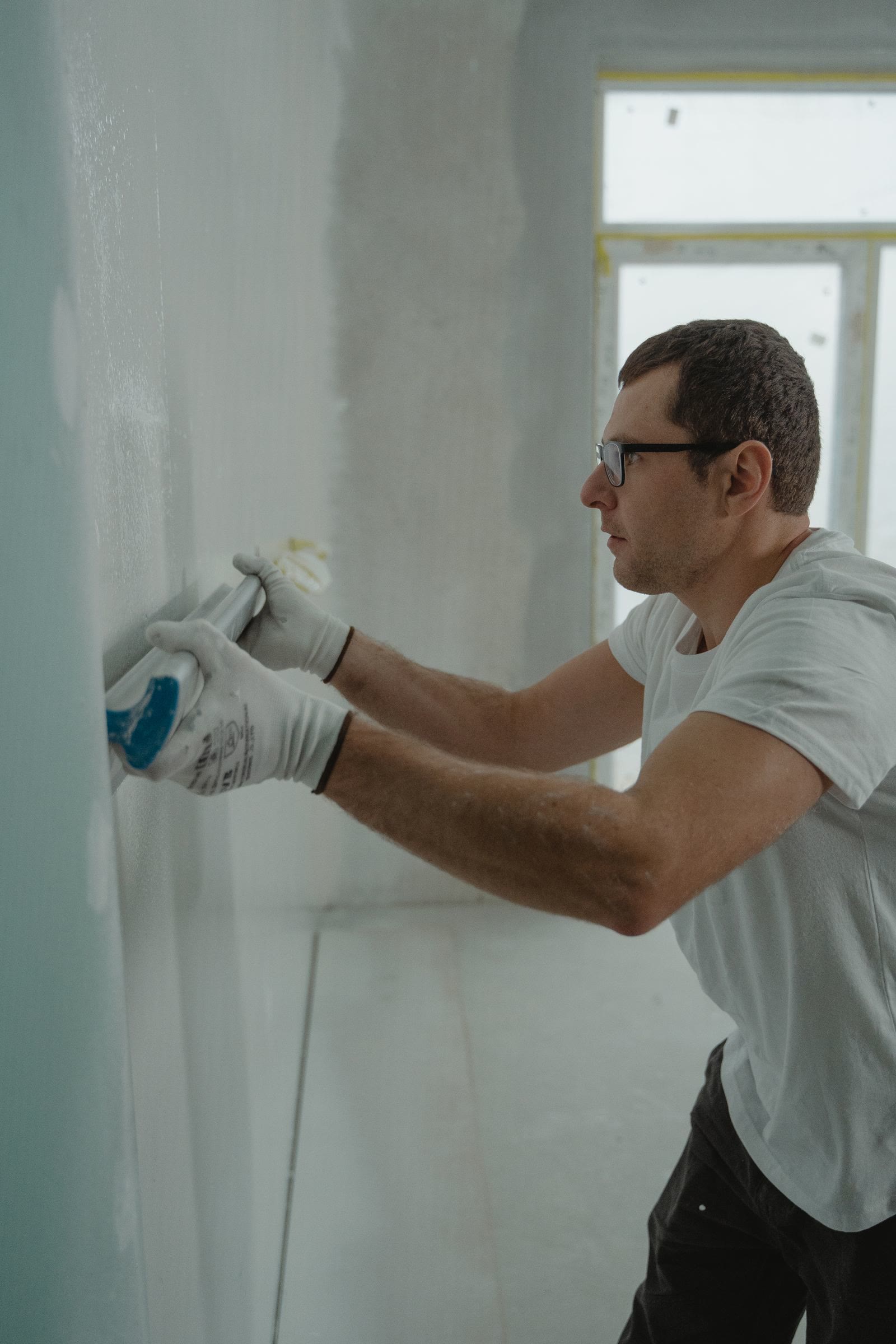 A plasterer skimming a wall with a wide trowel in a room under renovation