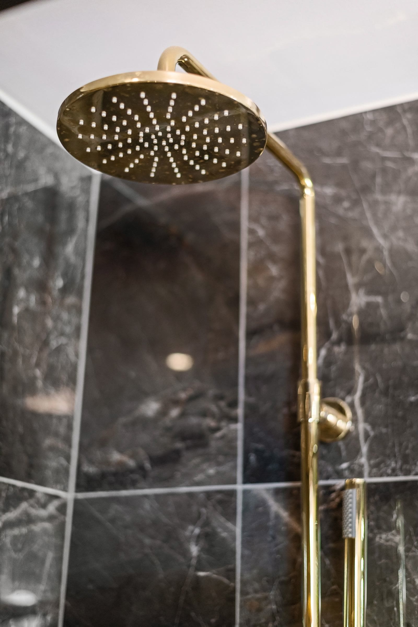 A gold shower head against dark marble tiles